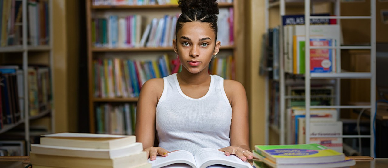  Teen girl in white tank top at the library studying to get into college. 